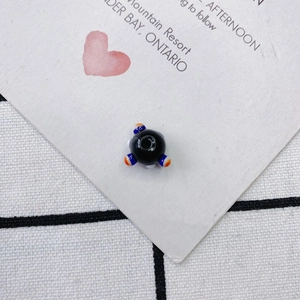 Vista detallada de una cuenta de vidrio negro hecha a mano con puntos coloridos para joyas DIY