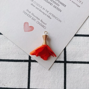 Detalle de colgante de rosa de tela naranja con tapa dorada y gancho para joyería artesanal