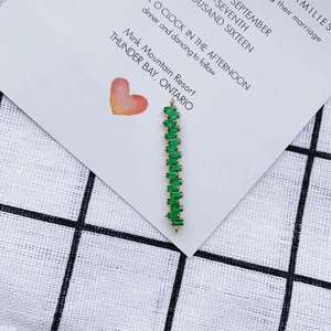 Detalle de colgante de barra dorada con circonitas verde esmeralda y dos anillas de conexion