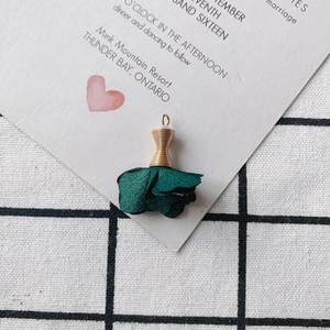 Detalle de un colgante de rosa en tela verde oscuro con capuchón de metal dorado
