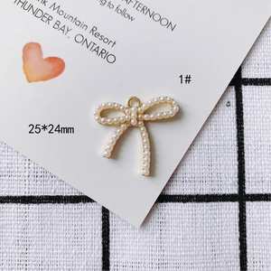 Vue macro d'un pendentif nœud doré de 25x24mm avec perles blanches et anneau de suspension