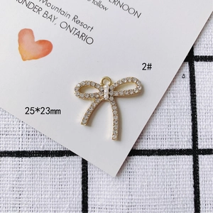 Détail d'un pendentif nœud doré avec cristaux sertis et trois perles, taille 25x23mm