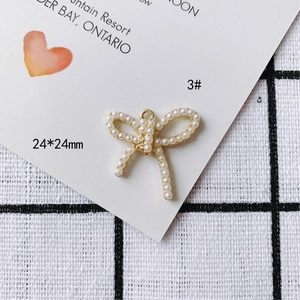 Vue macro d'un pendentif nœud doré 24x24mm orné de perles blanches sur fond sobre