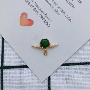 Detailansicht eines goldenen Ohrringanhängers in Flügelform mit grünem Edelstein