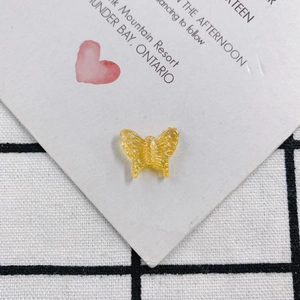 Detail of yellow translucent resin butterfly charm with embossed dots on checkered cloth