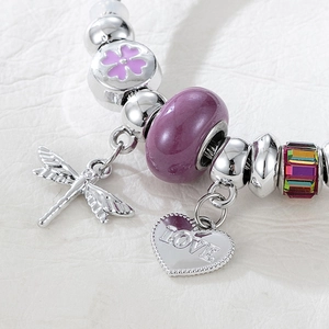 Detailed close-up of dragonfly and heart charms on a silver beaded charm bracelet
