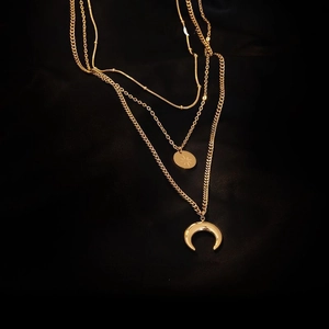 Close-up of triple-layered gold necklace with star-engraved coin and crescent moon pendant