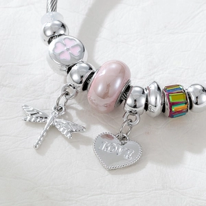 Detail of silver dragonfly and heart charms with pink beads on a textured white surface