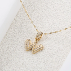 Dettaglio macro del ciondolo a lettera W in oro con pavé di zirconi scintillanti su catena