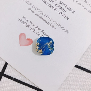 Nahaufnahme eines quadratischen blauen Harzanhängers mit Goldfolie und Trockenblume