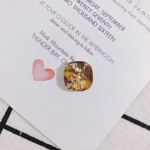 Nahaufnahme von quadratischem Harzanhänger in Braun mit Goldfolie und weißer Trockenblume