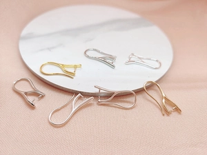Dettaglio di ganci per orecchini fai-da-te in oro e argento su marmo e tulle rosa