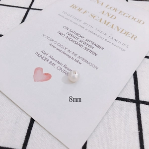 Detail shot of 8mm iridescent white pearl bead with drill hole on a white wedding card