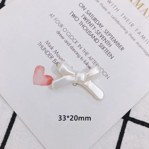 Close-up of pearl white bow charm with dimensions 33x20mm on a stylish plaid fabric