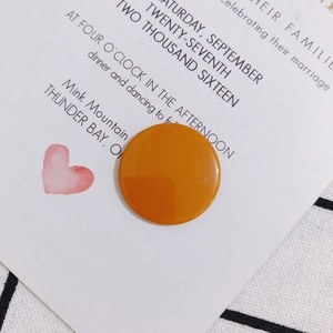Primer plano de un dije circular de acrílico naranja brillante sobre fondo de tarjeta