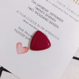 Macro shot of polished burgundy resin triangle charm on aesthetic stationery background