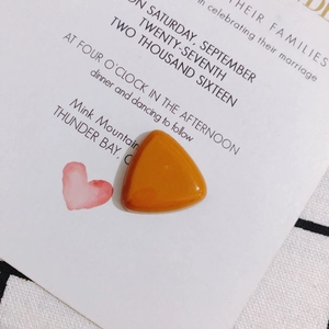 Macro detail of amber resin triangle pendant on a white card with pink heart illustration