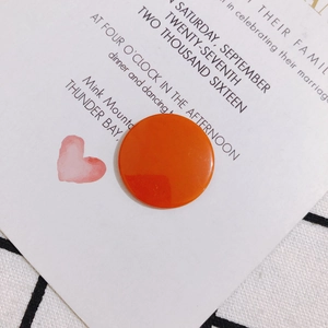 Primer plano de un disco acrílico naranja brillante para joyas DIY sobre una invitación blanca