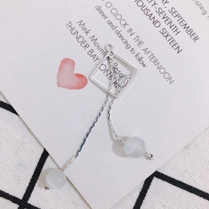 Détail de boucles d'oreilles argentées à pompons, pierres œil de chat et zircon