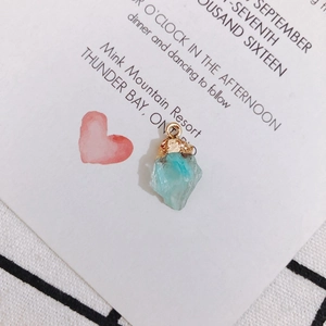 Macro shot of an irregular light blue crystal pendant with a gold hook on white card