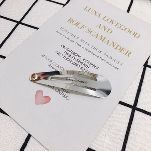 Close-up of a silver metal snap hair clip on a white decorative card backdrop