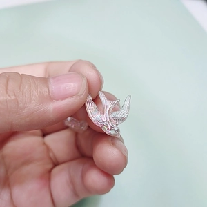 Macro view of a tiny iridescent swallow bird pendant held by hand for jewelry DIY