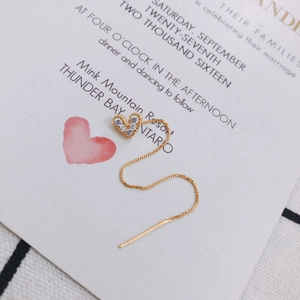 Detail eines goldenen Herz-Ohrrings mit Zirkonia-Pavé und feiner Kette auf einer Hochzeitskarte