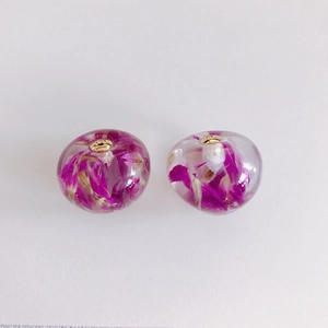 Dettaglio macro di orecchini in resina con veri fiori secchi viola e perni in metallo oro