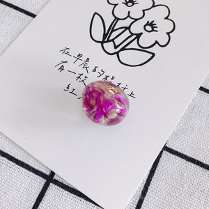 Dettaglio di un ciondolo in resina con fiori secchi veri e un anello in metallo dorato