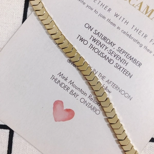 Close-up of a polished gold herringbone chain link bracelet on a textured card background
