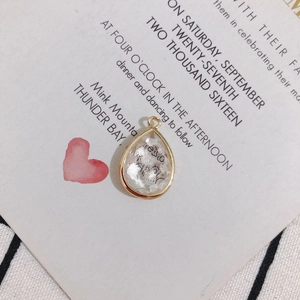 Close-up of teardrop-shaped pendant with gold metal edges and white shell fragments