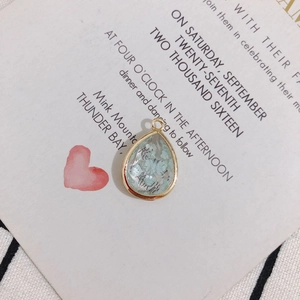 Detailed view of teardrop pendant with gold copper edging and blue dried flowers