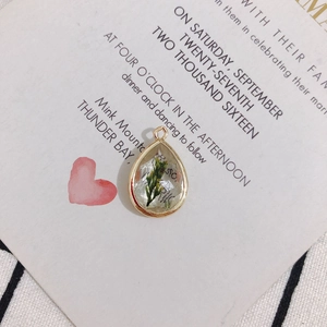 Detailed view of water drop resin pendant with green dried flower in gold frame