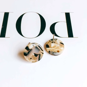 Macro view of round acetate earrings featuring tortoiseshell marble patterns and steel pins
