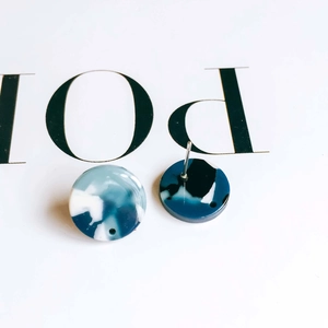 Macro shot of circular acetate earrings with blue marble texture on white display card