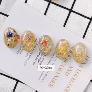 Détail macro du pendentif ovale en résine 20x30mm avec fleurs séchées et feuilles d'or