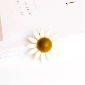 Primer plano de dije de margarita blanca con centro amarillo sobre un libro blanco
