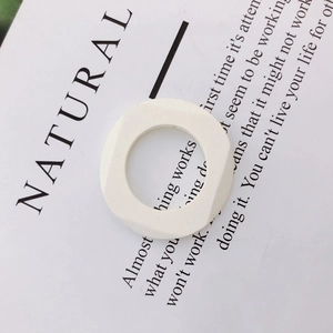 Macro detail of a white geometric square ring charm with a smooth matte finish on paper