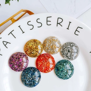 Détail macro de breloques en acrylique pailletées et feuilles d'or sur assiette blanche