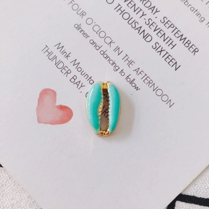 Detail of shell-shaped gold plated pendant with light blue enamel on artistic card