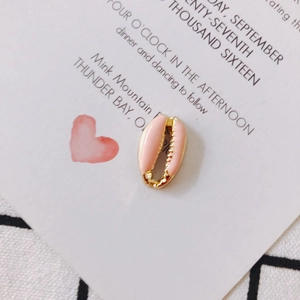 Macro shot of a pink enamel shell-shaped gold charm on a white card with heart pattern