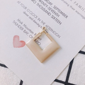 Détail d'une boucle d'oreille carrée géométrique dorée avec finition en émail