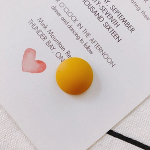 Macro shot of matte ginger yellow resin semicircle bead on a white invitation card