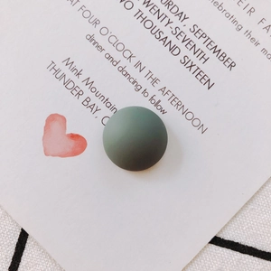 Detailed view of a dark green matte resin bead on an invitation card with pink hearts