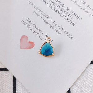 Dettaglio di un ciondolo a triangolo placcato oro con cristallo blu scuro e castone inciso