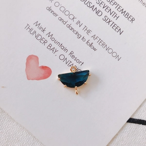 Dettaglio macro di un ciondolo a semicerchio placcato oro con cristallo blu e doppi anellini