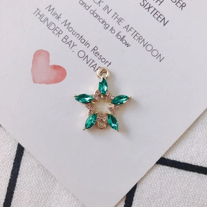 Macro detail of star-shaped golden pendant with green marquise crystals and tiny rhinestones
