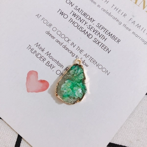 Detail of green teardrop druzy pendant with gold trim on an elegant paper background