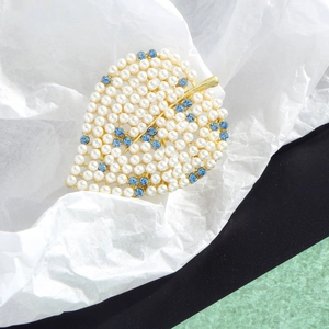 Elegant gold leaf brooch with white pearls and blue rhinestones on a textured background
