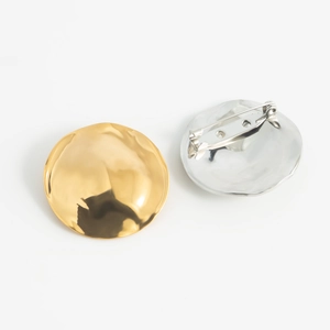 Minimalist disc-shaped metal brooch with hammered texture in 18K gold and silver finishes
